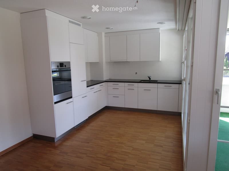 Modern kitchen with white cabinets, black countertops, wooden flooring, and stainless steel oven and sink.