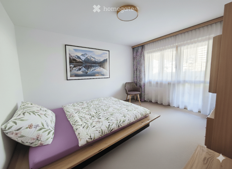 Cozy bedroom with a wooden bed frame, purple bedding, a small wooden chair, and a large picture frame on the wall.