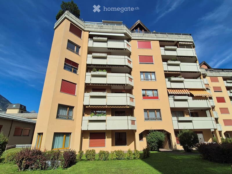 Multi-story residential building with balconies, windows, and greenery in front.