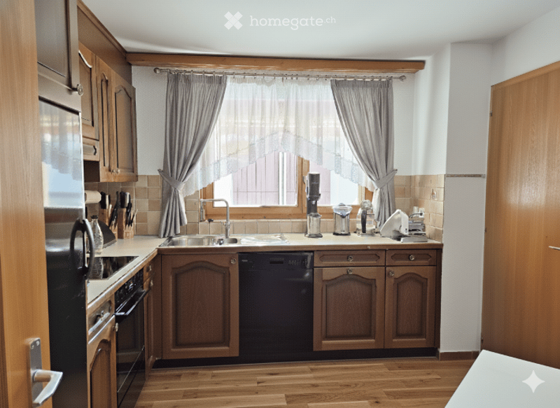 A well-equipped kitchen with wooden cabinets, stainless steel appliances, a window with curtains, and a sink with a faucet.