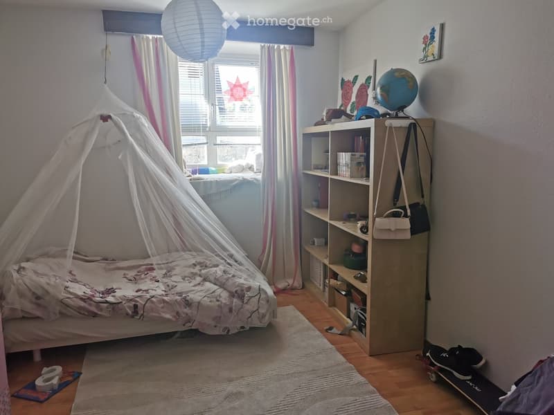 Cozy bedroom with a bed covered in a floral duvet, a bookshelf filled with books and decorative items, a globe, and a hanging paper lantern. A skateboard and shoes are placed near the door.