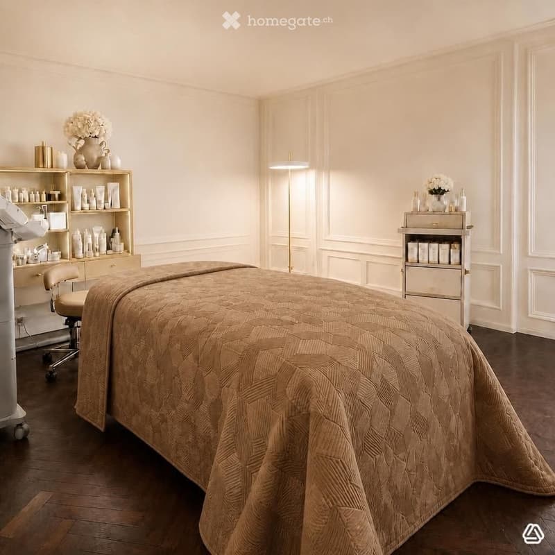 A well-lit, elegant spa treatment room with a large treatment table covered in a beige quilted blanket, surrounded by shelves holding various skincare products, a vase with white flowers, a floor lamp, and a small chair.