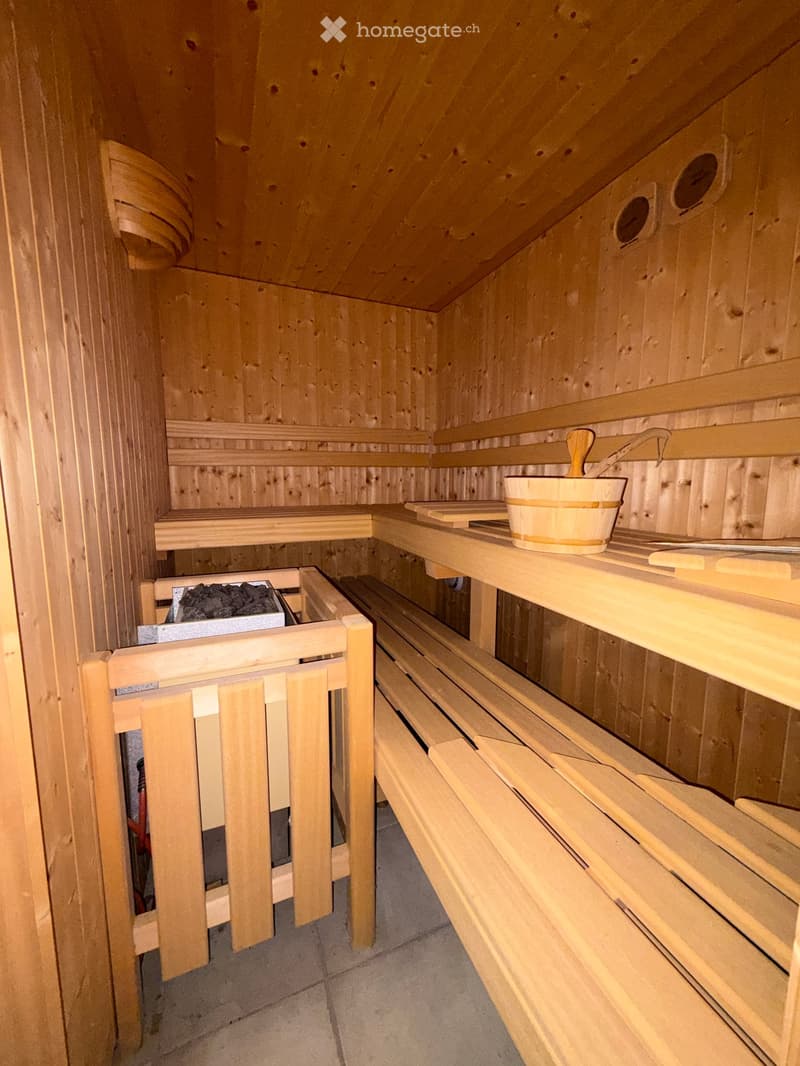 Wooden sauna with benches, a bucket, and a paddle on a shelf.
