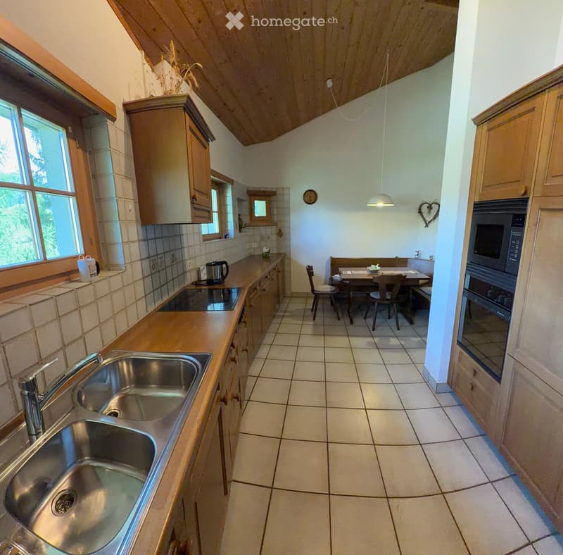 Bright kitchen with wooden cabinets, stainless steel sink, oven, microwave, and a small dining area with a table and chairs.