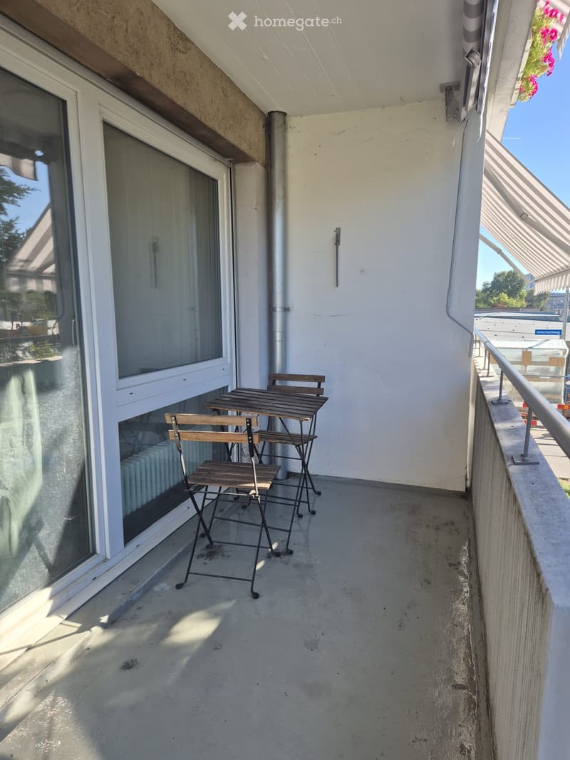 Balcony with a small table and four chairs, large windows, and a metal railing.