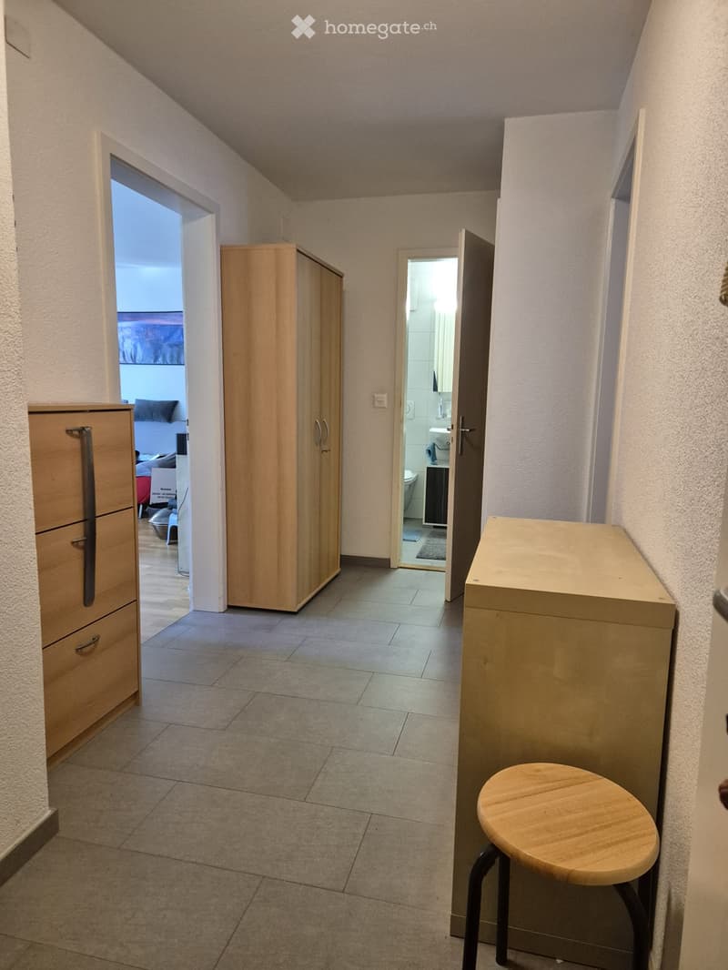 A narrow hallway with tiled flooring, light-colored walls, and several doors leading to different rooms, including a bathroom and a bedroom.