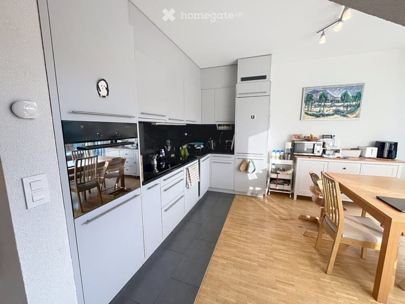 Modern kitchen with white cabinets, stainless steel appliances, and a wooden dining area.