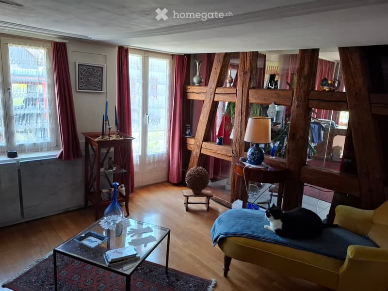 Living room with wooden floor, large windows, sofa, coffee table, table lamp, decorative vases, and a cat on the sofa.