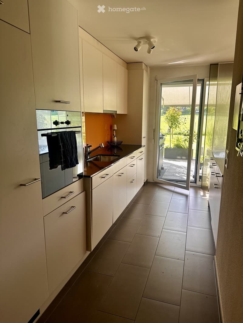 Modern kitchen with white cabinets, stainless steel sink, and an open sliding door leading to a patio.