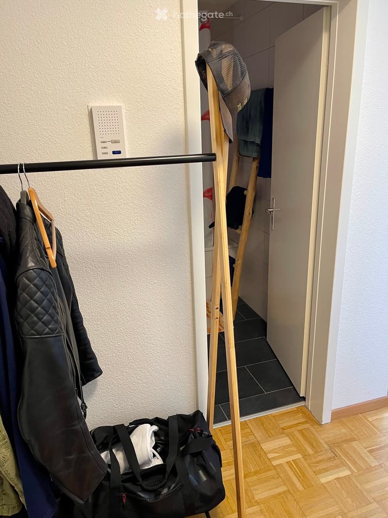 Hallway with wooden floor, coat rack, open closet, and various clothing items and bags.