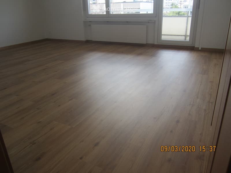 Empty room with wooden flooring, large window, radiator, and sliding glass door leading to a balcony.