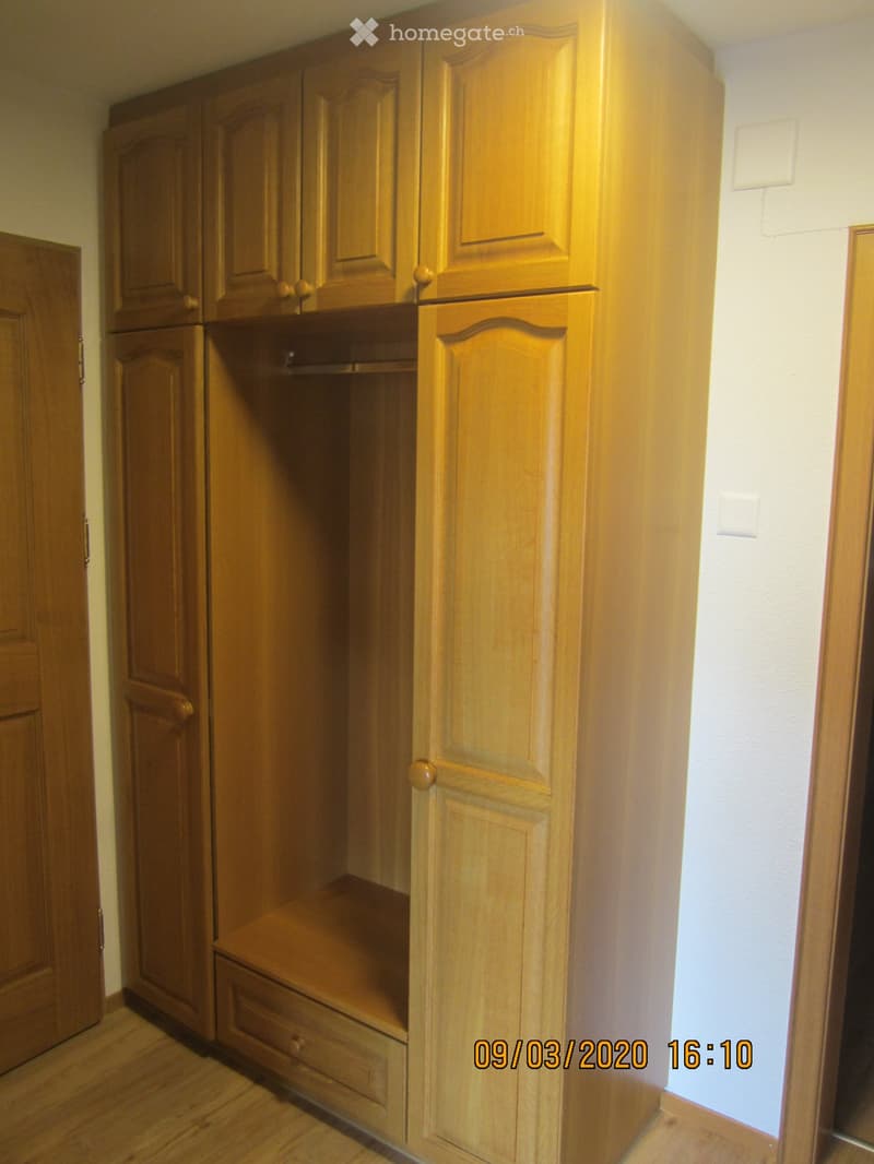 Empty wooden closet with multiple doors and drawers, light-colored walls, and wooden flooring.