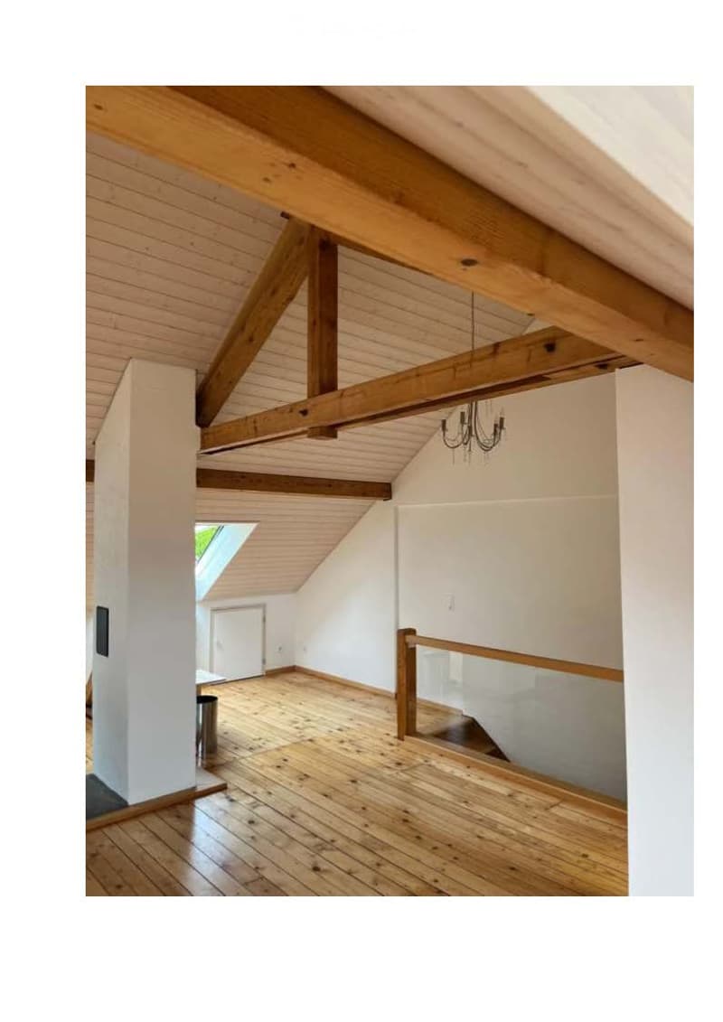Empty room with wooden floors, exposed wooden beams, white walls, and a small skylight window.