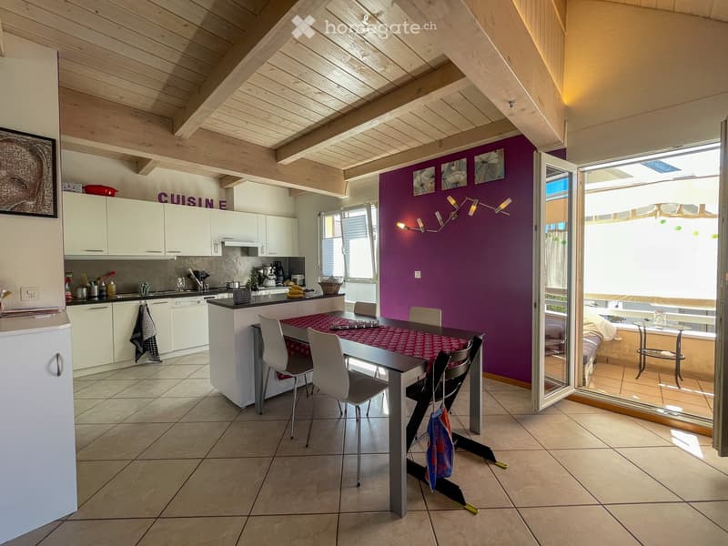 Modern kitchen with white cabinets, a central island, and a dining area. The space features a purple accent wall, exposed wooden beams, and large windows with blinds.