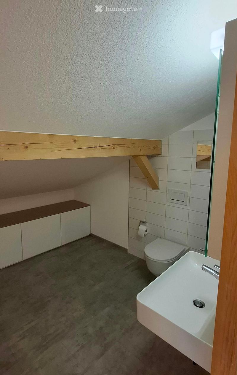 Modern bathroom with a white sink, toilet, and wooden cabinet. Features a large mirror and tiled walls.