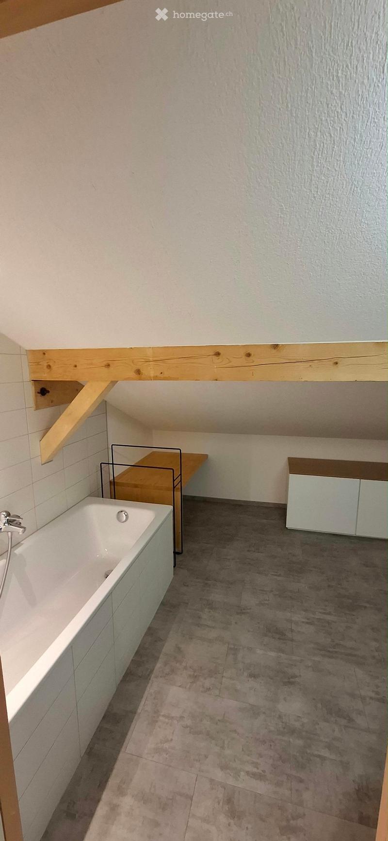 Modern bathroom with a white bathtub, wooden table, and light-colored cabinet.
