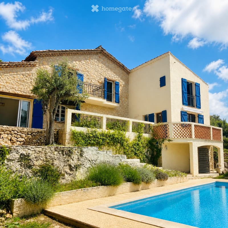 Two-story stone house with blue shutters, balconies, and a swimming pool in the garden.
