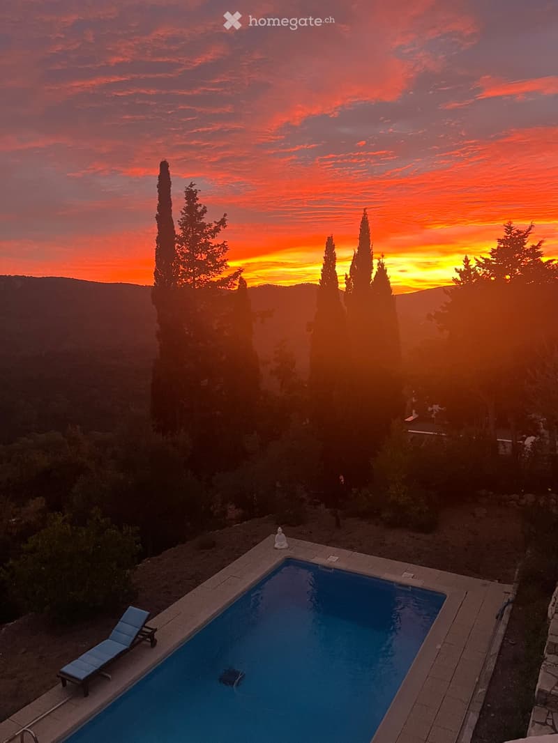 A swimming pool with lounge chairs, overlooking a scenic valley at sunset.