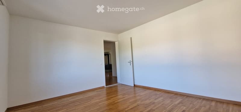 Empty room with light-colored walls and wooden flooring, featuring two open doors leading to adjacent spaces.