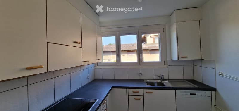 Modern kitchen with white cabinets, tiled backsplash, and a window overlooking a residential area.