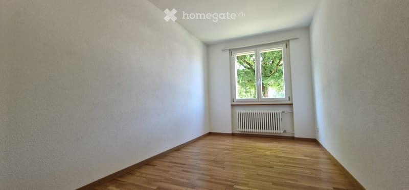 Empty room with wooden flooring, white walls, and a single window with a radiator below it.