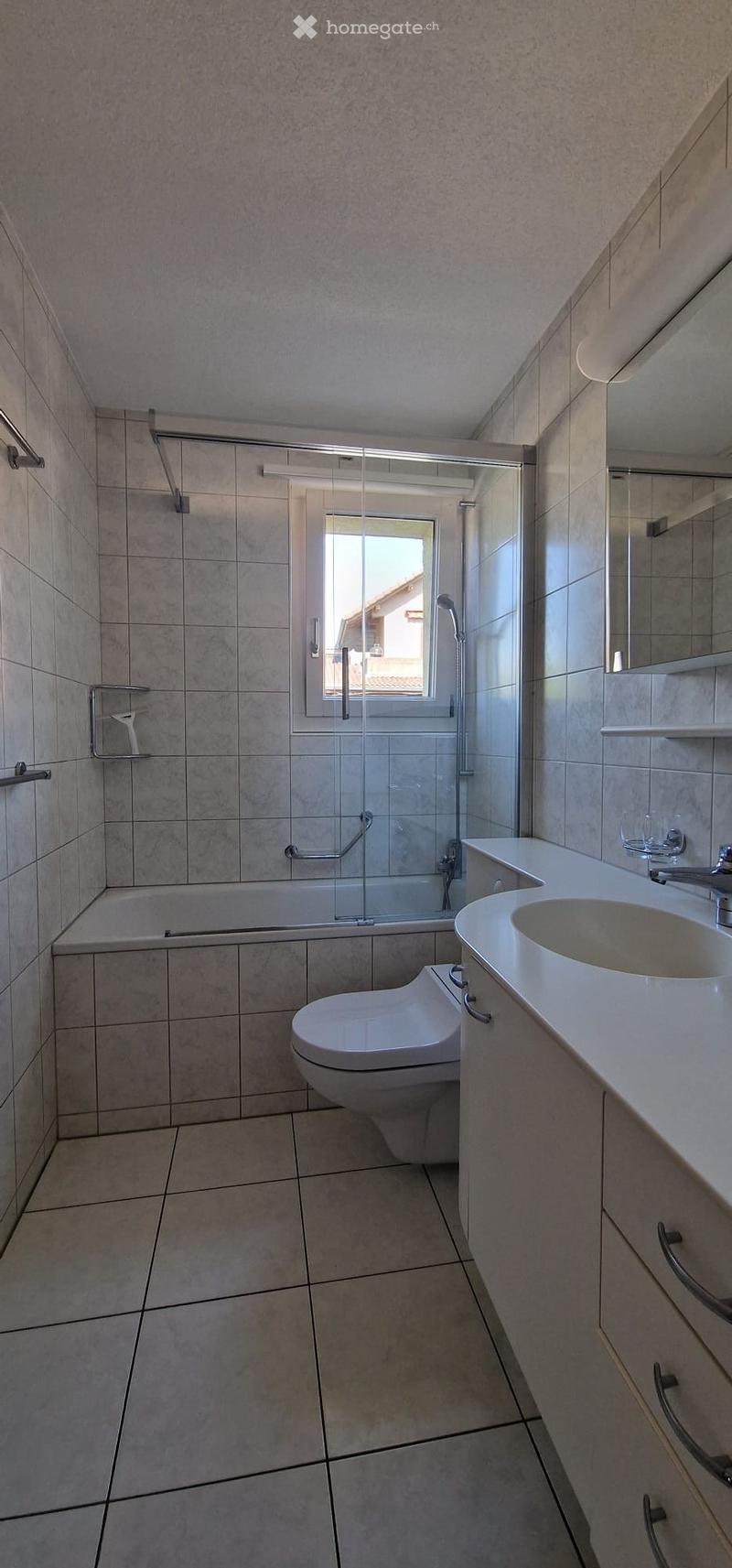 Modern bathroom with tiled walls and floor, featuring a bathtub, toilet, sink, and shower area with a glass enclosure.