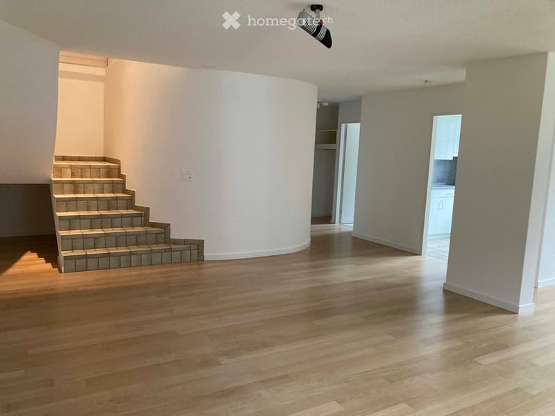 Empty room with wooden flooring, a staircase leading upwards, and a doorway to another room.