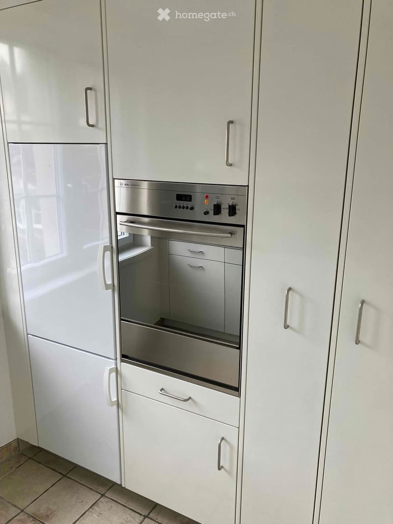 Modern kitchen with white cabinets, stainless steel oven, and refrigerator. The oven has a digital display and multiple control knobs.