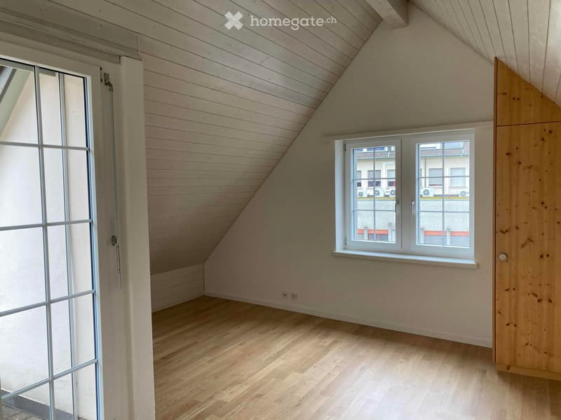 Empty attic room with wooden floors, slanted wooden ceiling, large windows, and a glass door leading to a balcony.