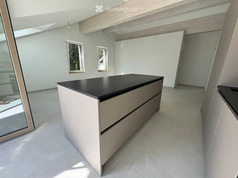 Modern kitchen with a sleek black countertop kitchen island, light-colored cabinets, and large windows allowing natural light to fill the space.