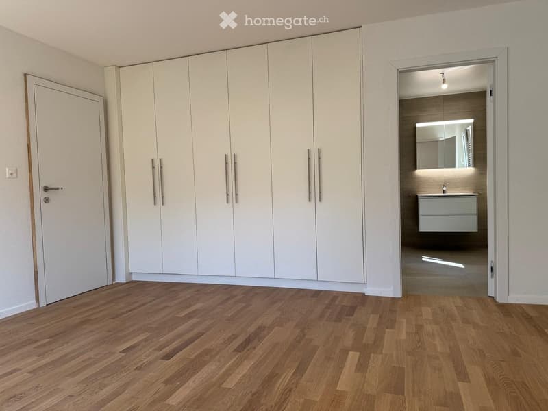 Empty room with light-colored wooden flooring, white built-in wardrobes, and an open doorway leading to a modern bathroom.
