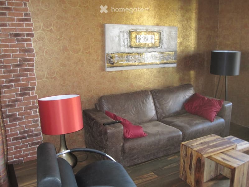 Living room with a gray leather sofa, red cushions, a wooden coffee table, a black chair, and two lamps.