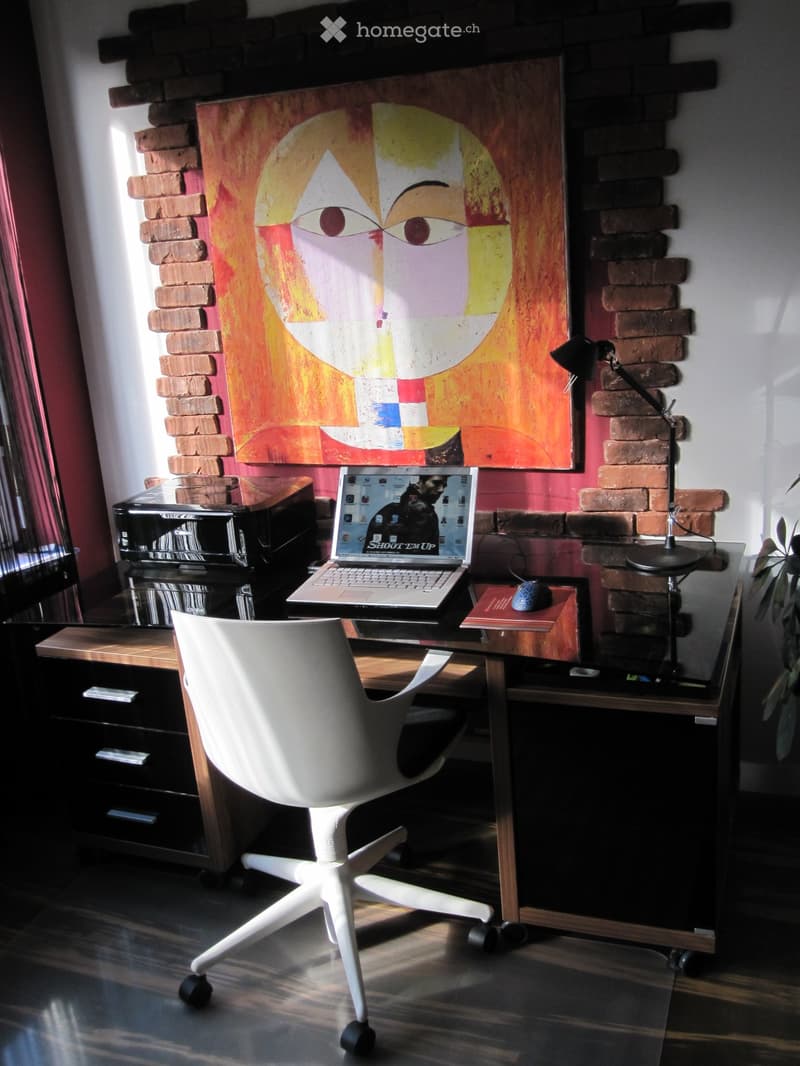 Modern office space with a white ergonomic chair, glass desk, laptop, lamp, printer, and artwork on the wall.