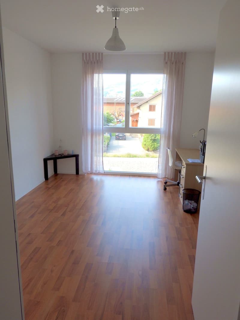 Bright, unfurnished room with wooden flooring, large windows, and a small desk setup.