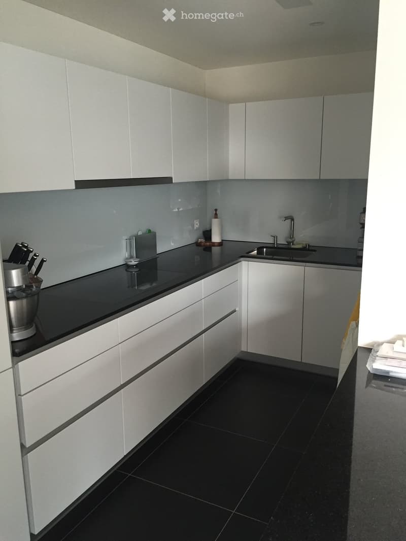 Modern kitchen with white cabinets, black countertops, and black tiled floor. Includes a sink, faucet, blender, knives, and a paper towel holder.