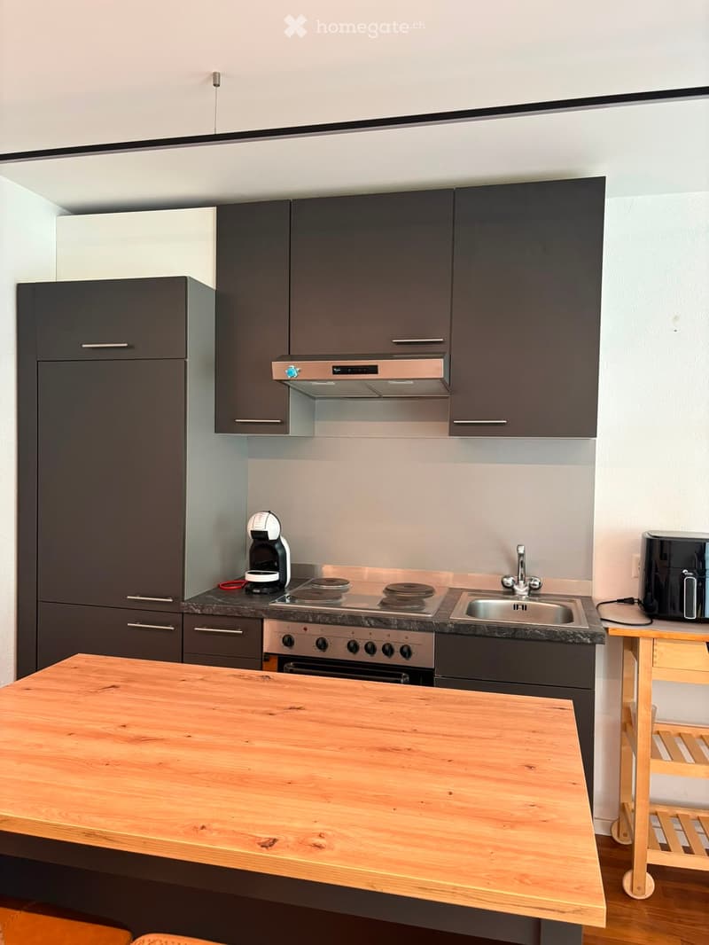 Modern kitchen with dark grey cabinets, stainless steel appliances, and a wooden island table.