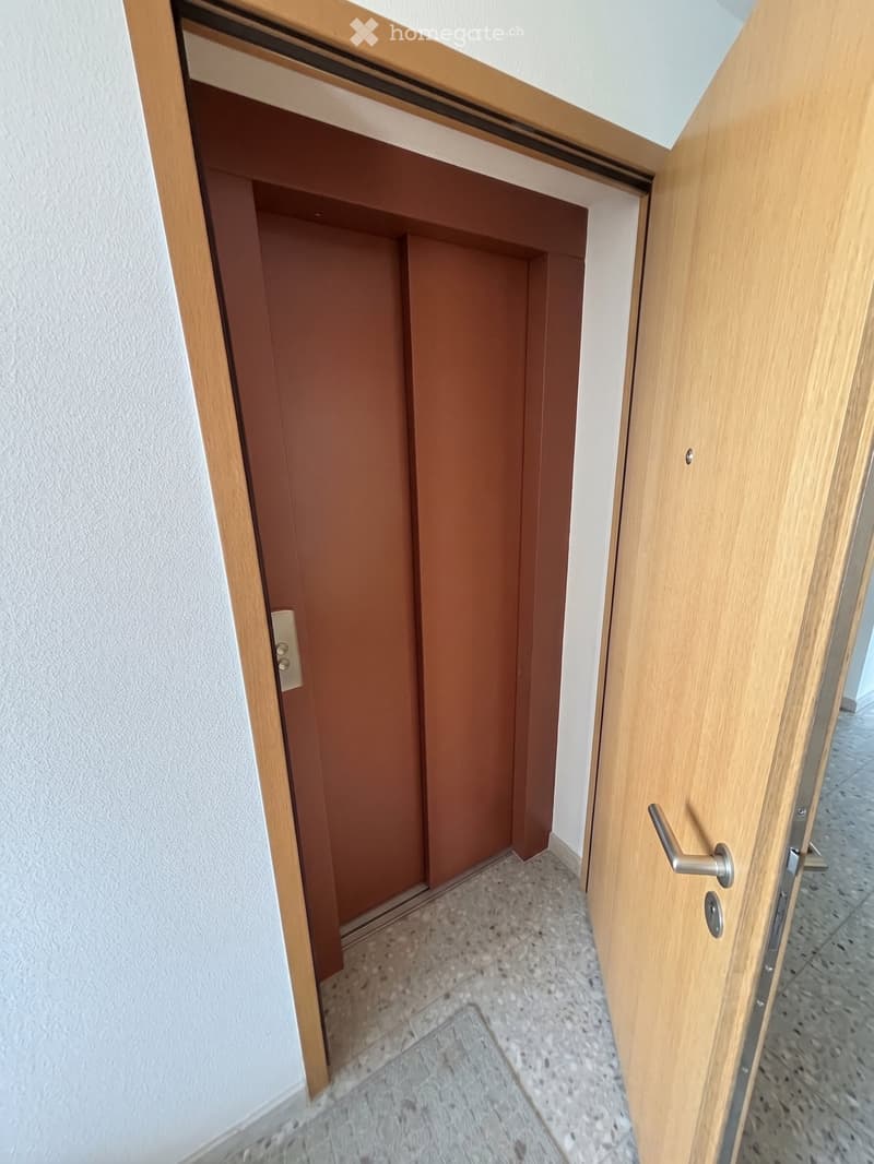 A narrow hallway with tiled flooring and wooden doors on both sides, featuring a partially open door on the right.