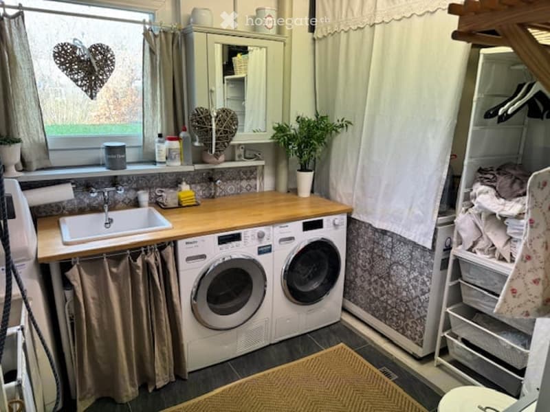Bathroom with a sink, washing machine, dryer, mirror, and cabinet. The space features a wooden countertop, tiled walls, and a window with a heart-shaped decoration.