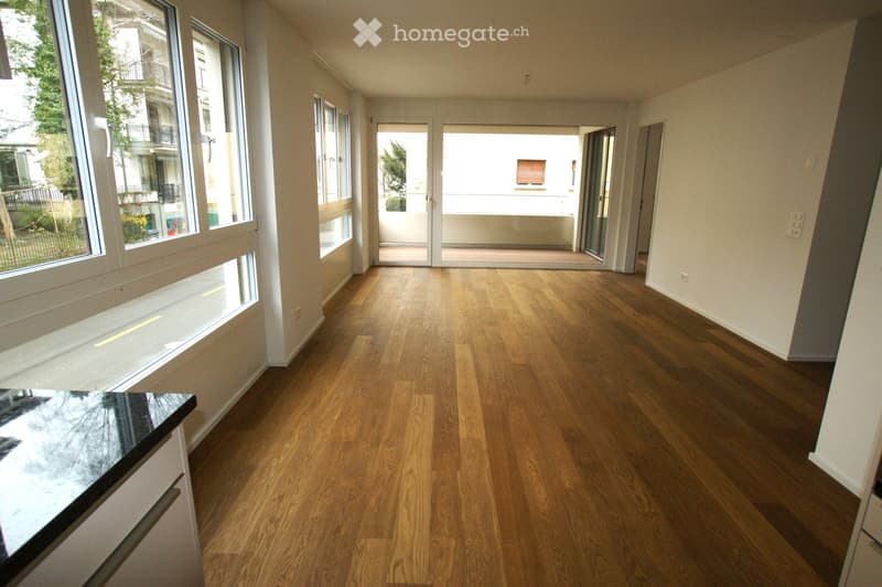 Empty room with wooden flooring, large windows, and a sliding glass door leading to a balcony area.