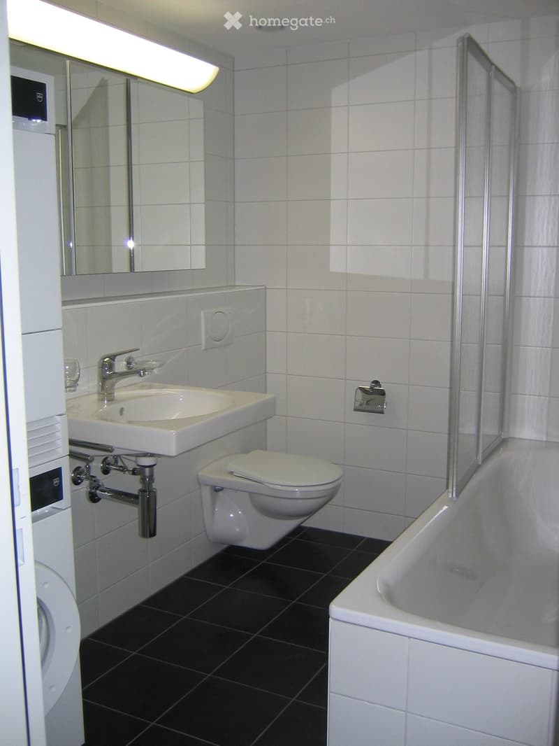 Modern bathroom with white tiles, black floor, sink, toilet, bathtub, and mirror.