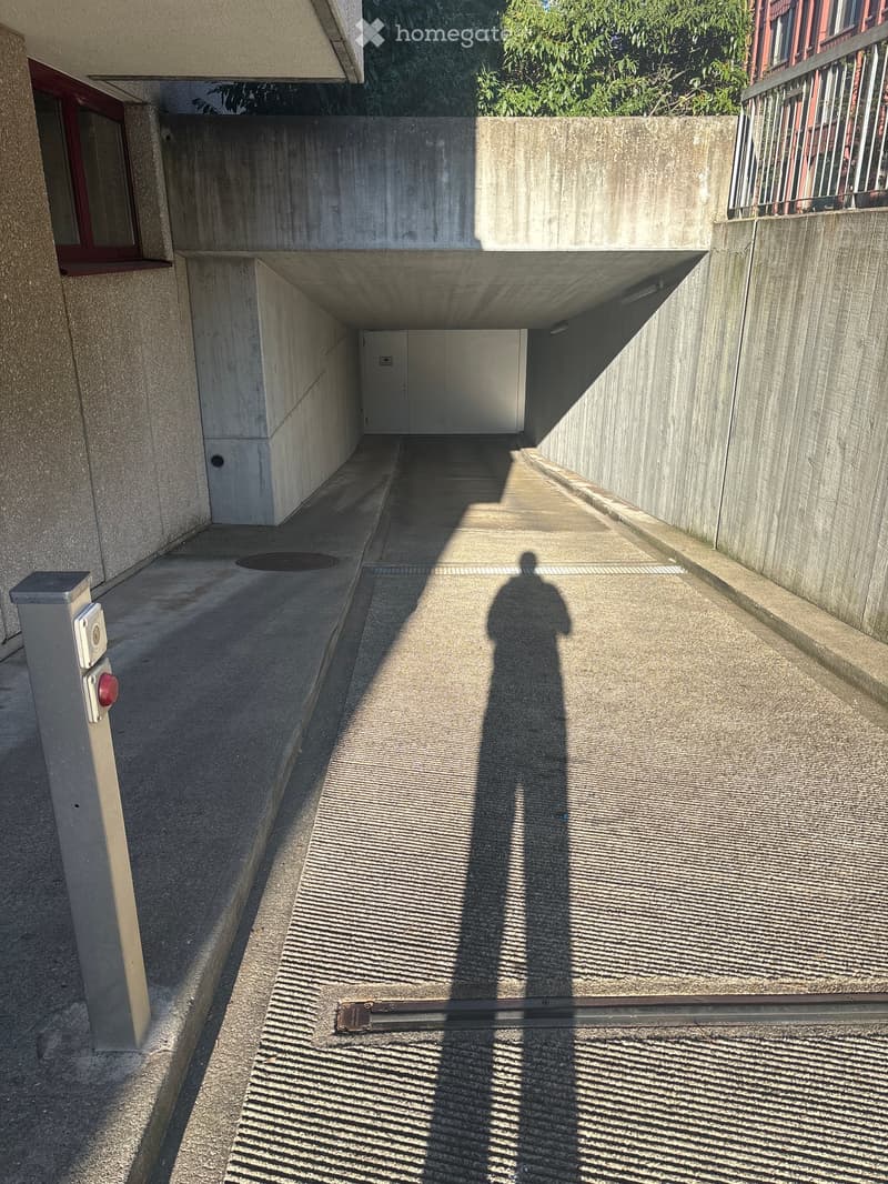 A narrow concrete corridor with a raised ground floor, featuring a manhole cover, a red button, and a white door at the end.