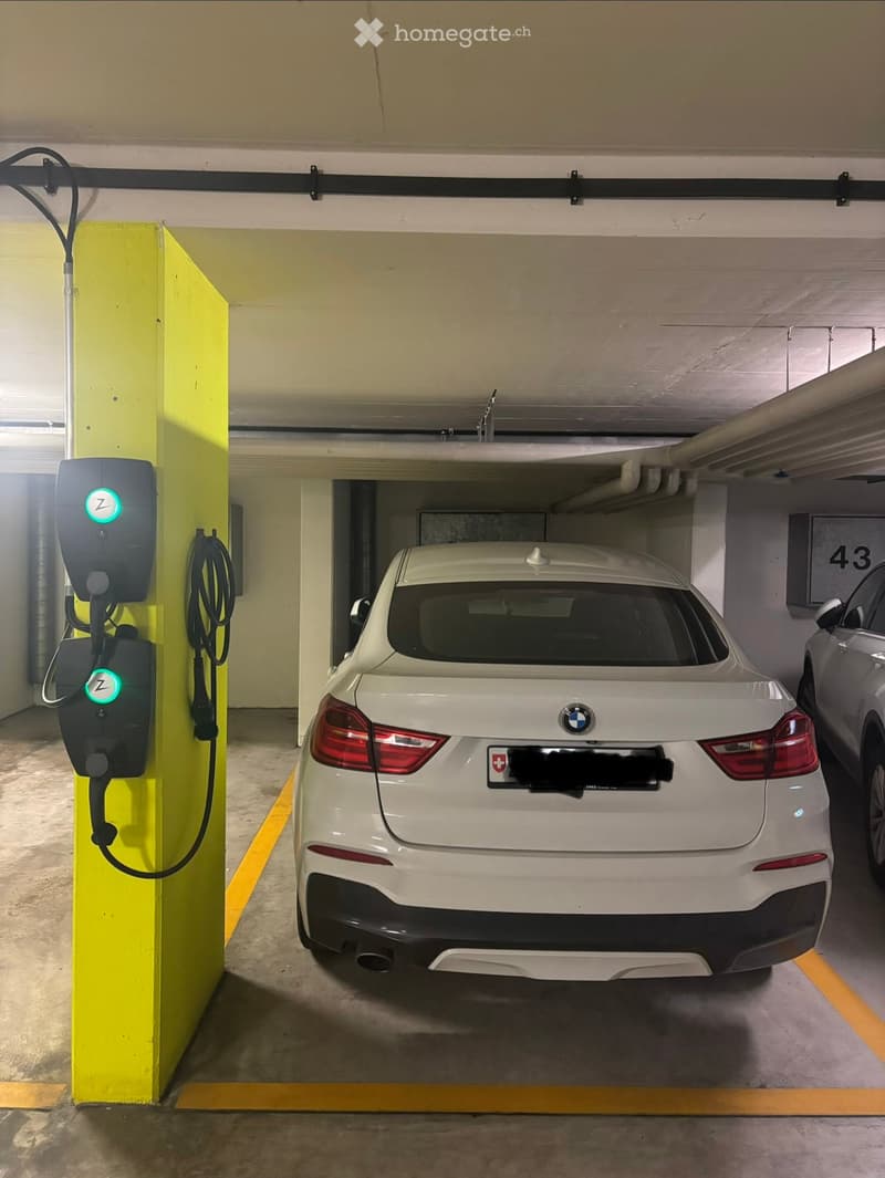 Underground parking area with a white BMW car parked next to a yellow electric charging station.