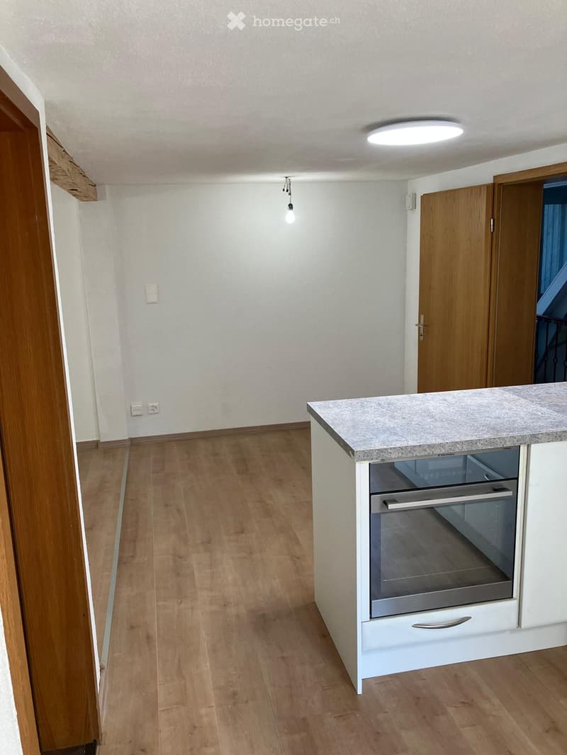 Modern kitchen with light wooden flooring, white cabinetry, and a built-in oven. The space is clean and well-lit with recessed ceiling lighting.