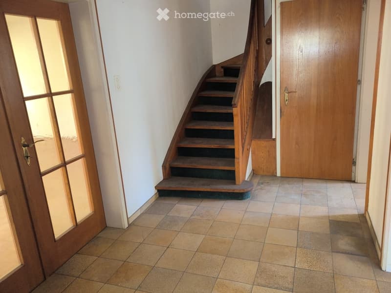 Hallway with tiled floor, wooden staircase, and two wooden doors, one with glass panels.