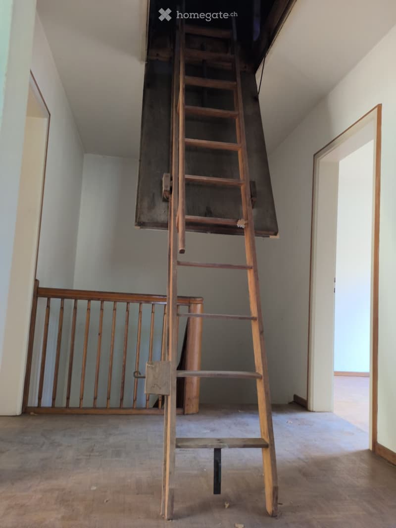 Empty room with wooden floor, white walls, and a wooden staircase leading to an attic space. No furniture or equipment is present.