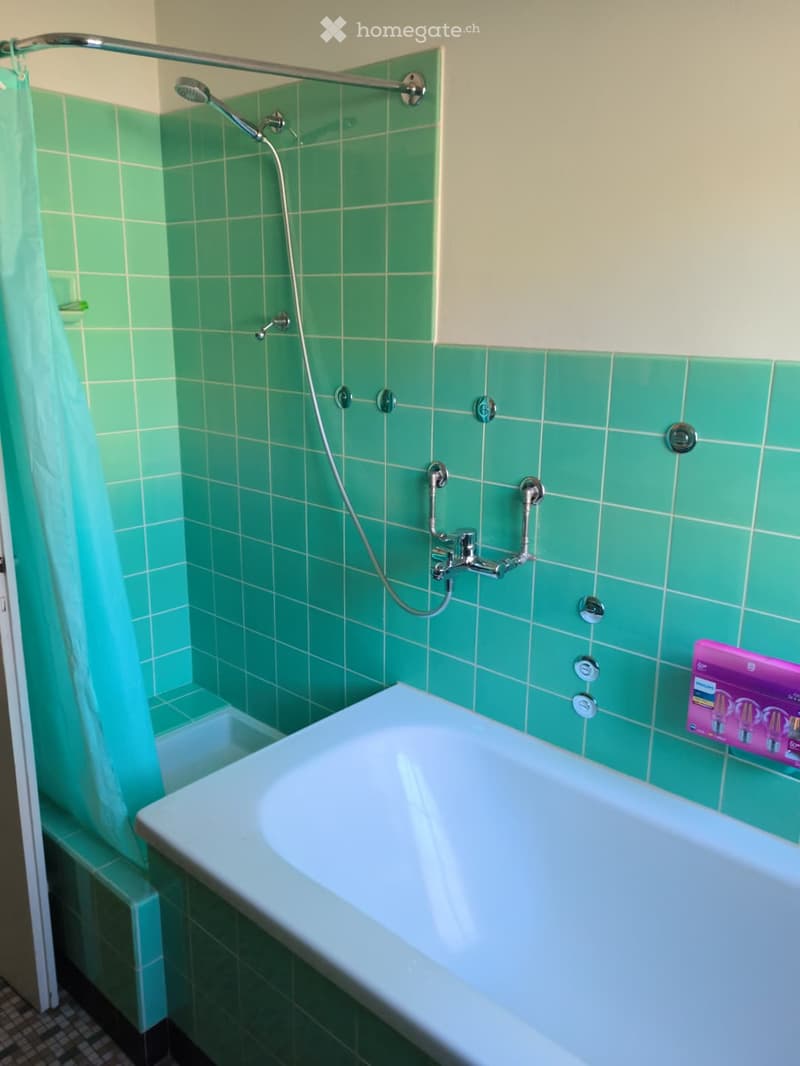 Bathroom with green tiled walls, a white bathtub, a showerhead, and a faucet.