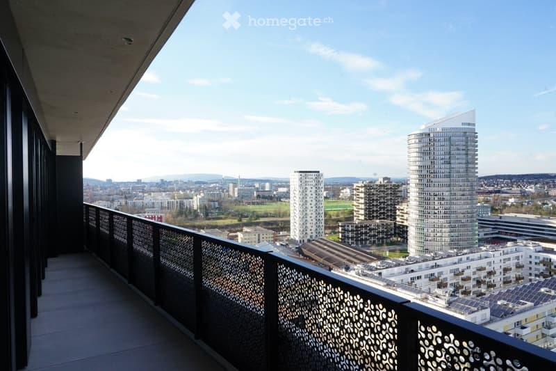 Balcony with modern metal railing, overlooking a cityscape with modern high-rise buildings and a clear blue sky.