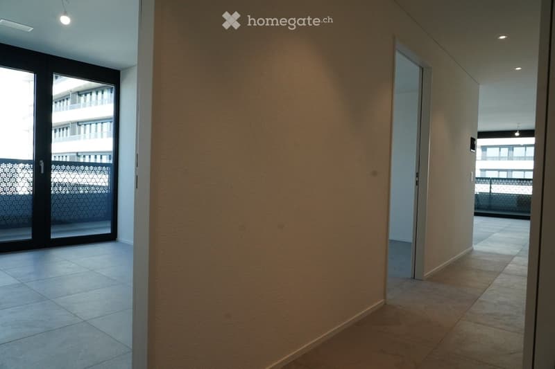 Empty hallway with tiled flooring, beige walls, and a sliding glass door leading to a balcony area.