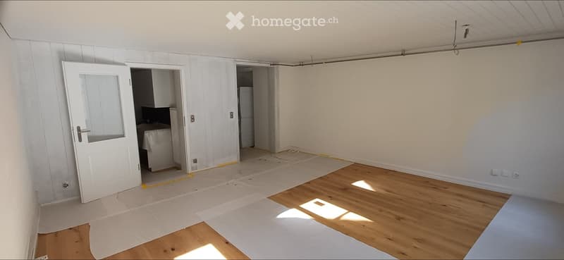 Empty room with wooden flooring, white walls, and a door leading to another room. No furniture or equipment is present.