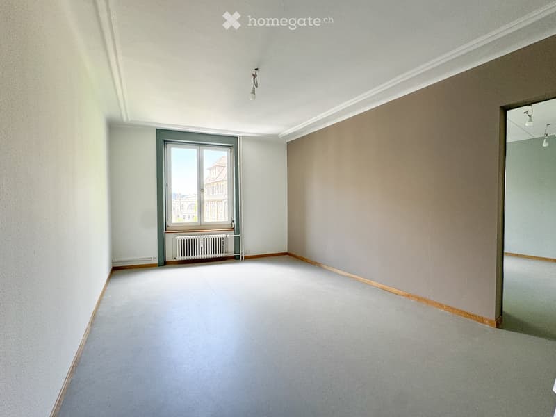 Empty room with light-colored walls, a window with a radiator below, and a door leading to another space.